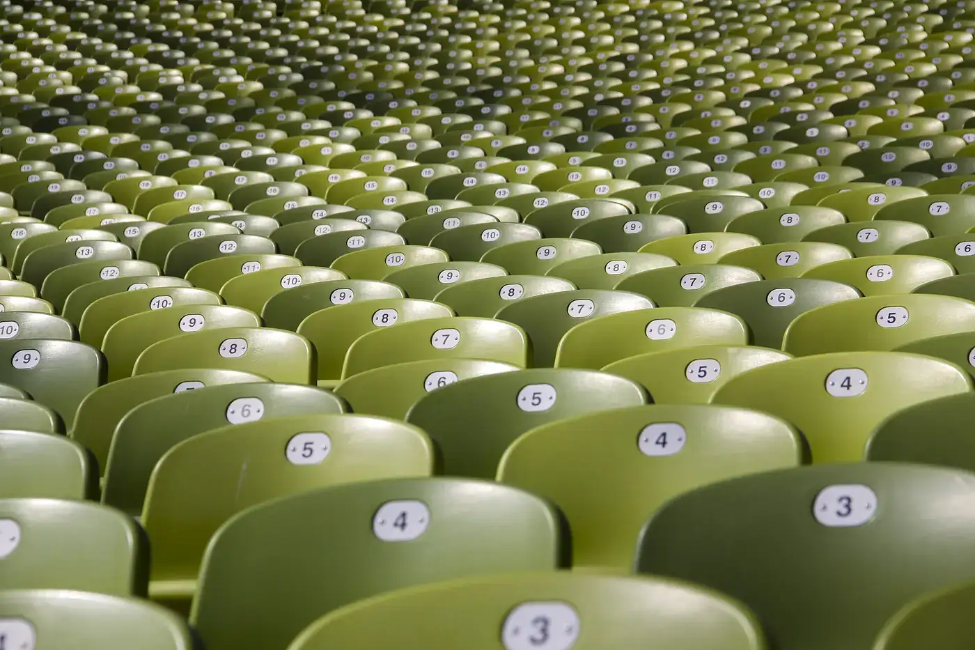 Bancadas de um estádio de atletismo vistas do interior, com a pista e a iluminação ao fundo.