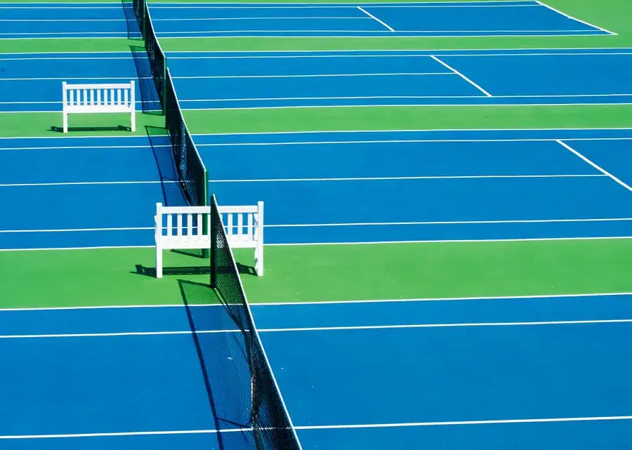 Campo de ténis com a rede montada e as linhas brancas marcadas, sem jogadores.