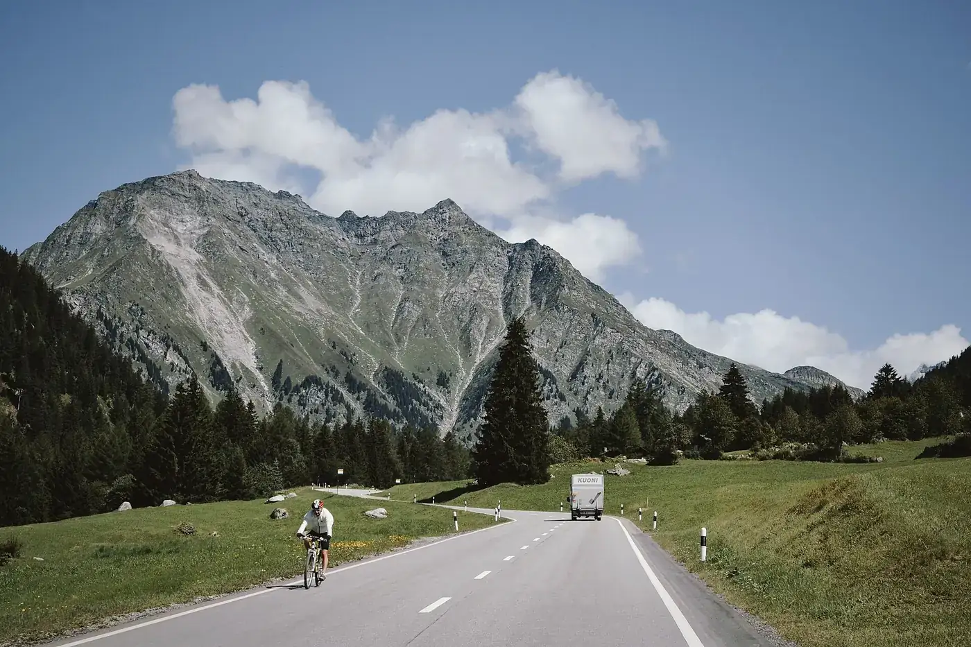 Ciclista a subir uma estrada de montanha estreita com o vale ao fundo.