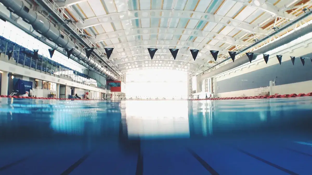 Piscina coberta de competição com raias marcadas e bandeirolas suspensas.