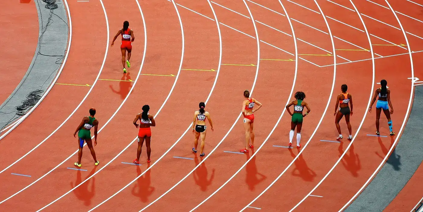 Atletas a correr em raias marcadas de uma pista sintética durante uma prova de velocidade.